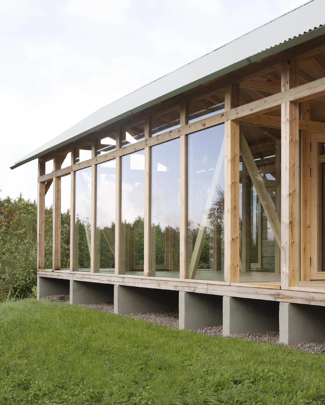 Detail of a timber-framed house with full-height glazing, raised on stone footings