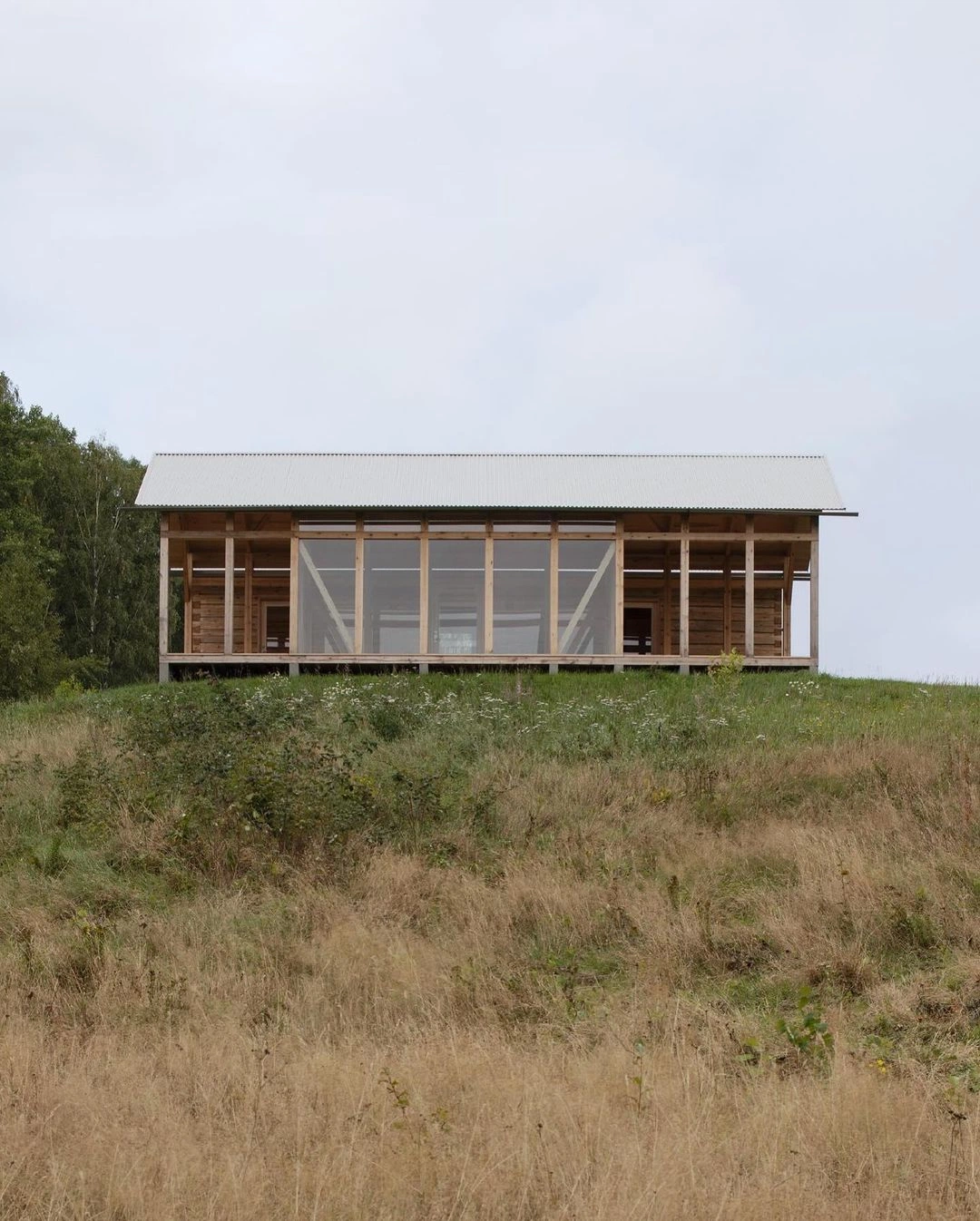A timber house standing alone on a grass ridge under an overcast sky
